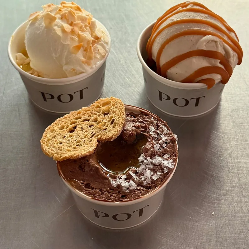 Tres vasos Pot sobre un mostrador: helado de yogur con coco tostado, helado de vainilla con caramelo salado y mousse de chocolate con sal y una tostada de pan